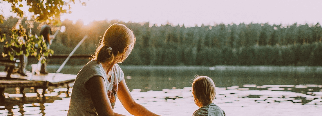 A woman and a toddler on the shore of a lake at sunset