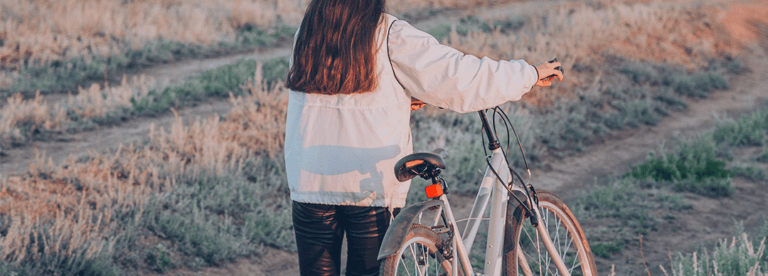 A young person in a white sweater walks through a field with a bicycle
