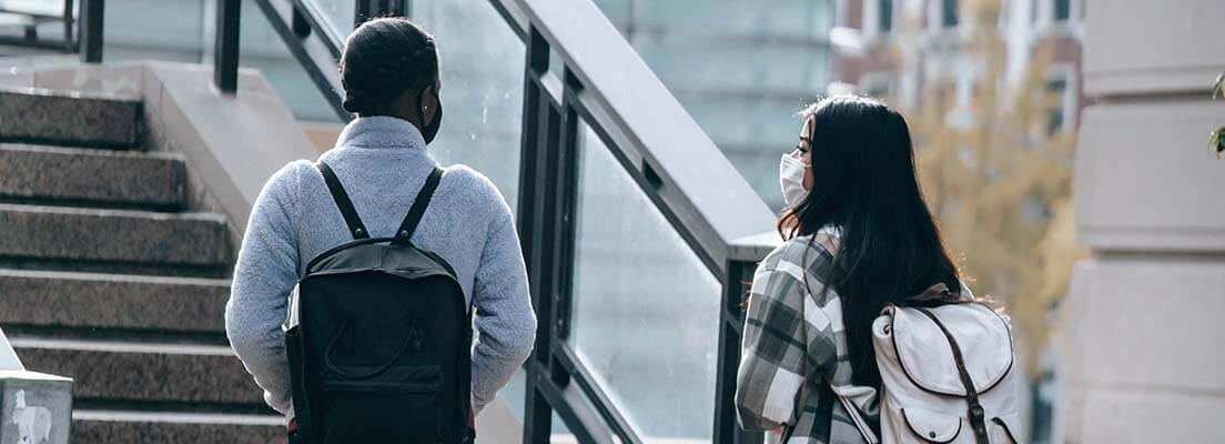 Photo of two students wearing facemasks and backpacks