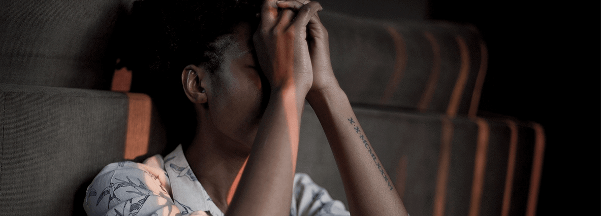 Image of a young woman seated with her face rested against her hands