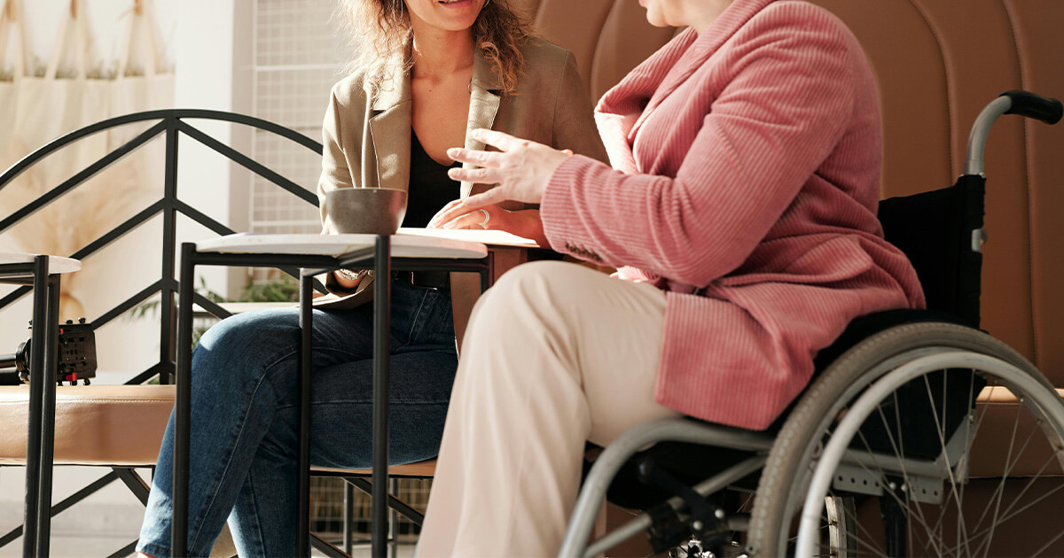 Two people sitting at a coffee shop, one is in a wheelchair.