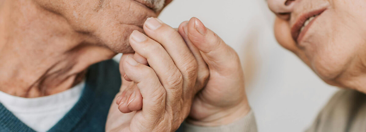 An older man holds and an older woman's hand and looks like he is about to kiss her hand.